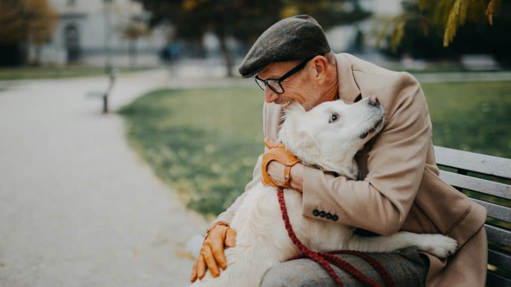 A man sitting on a bench and hugging his pet dog tightly.