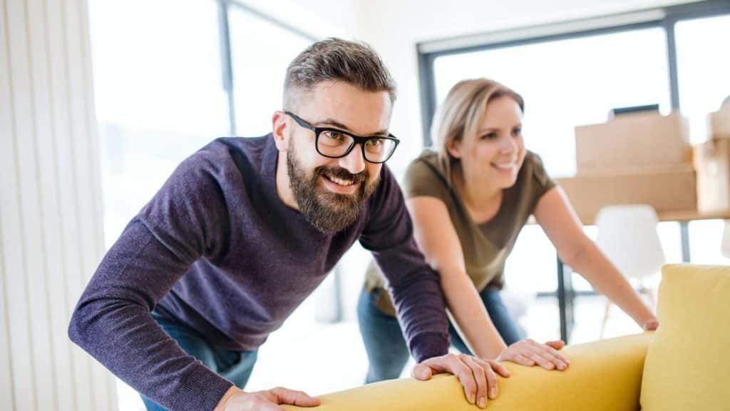 A man and a woman moving a yellow sofa together.