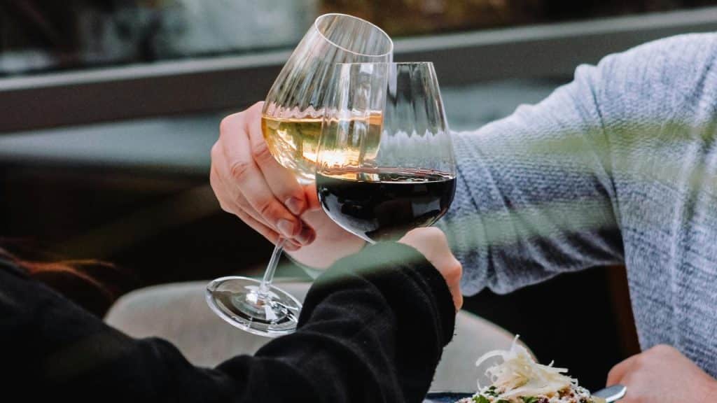 A pair of wine glasses is being clinked by two people at a restaurant table.