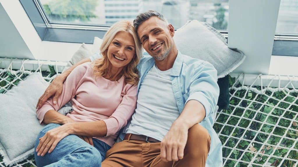 A mature couple smiling together while sitting on a netted sofa.