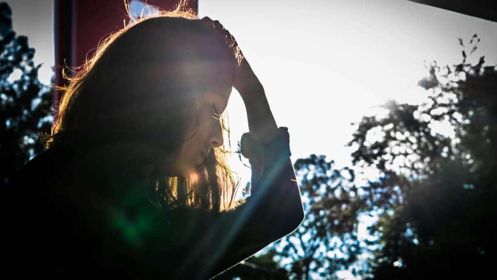 A woman sitting outdoors with her head resting on her hand in sunlight.