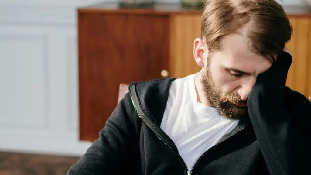 A man sitting indoors with his head resting on his hand.