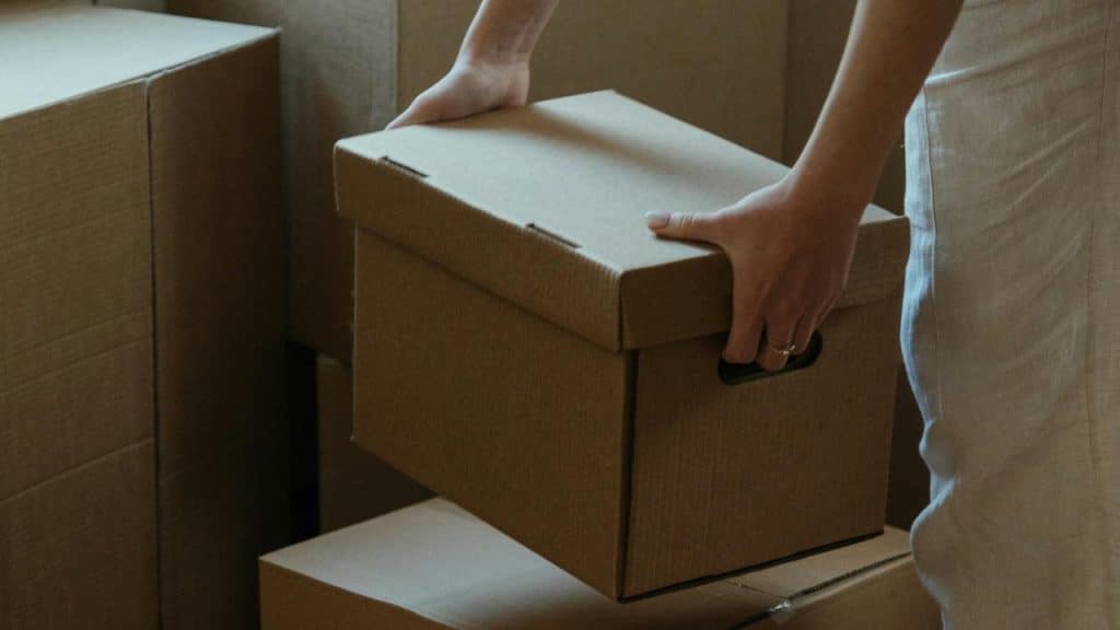 A person holding a cardboard box among other packed boxes.