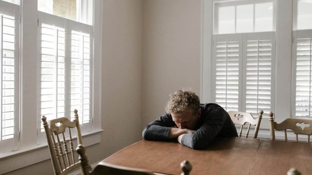 A man sitting alone at a table with his head resting on his arms.
