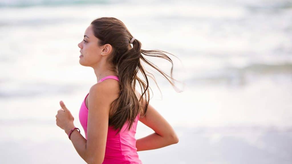 A woman jogging on the beach in a pink tank top.