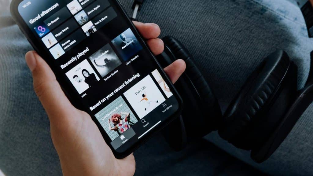 A person holding a smartphone showing a music app with headphones nearby.