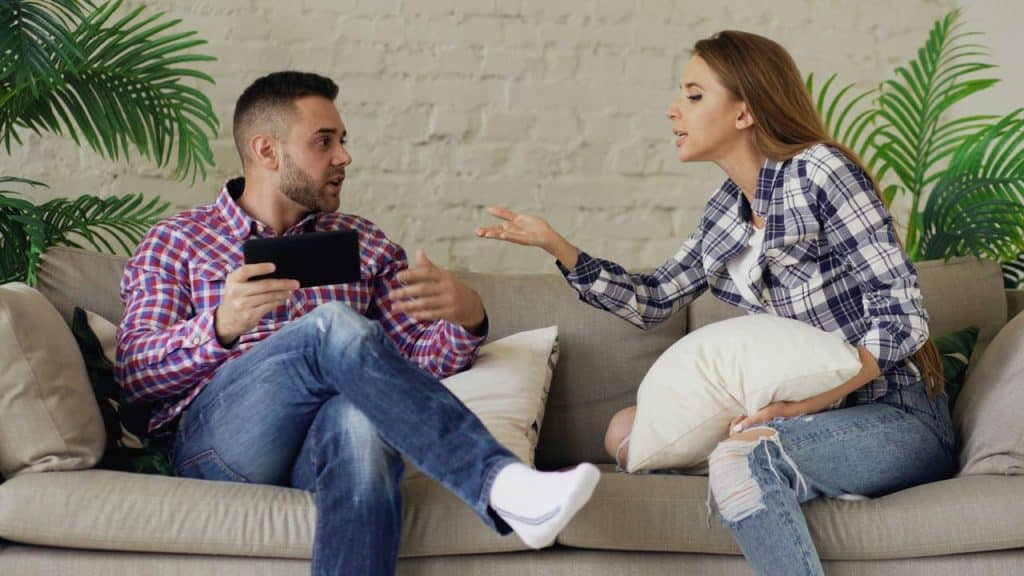 A man holding a tablet argues with a woman in a plaid shirt who is gesturing with one hand.