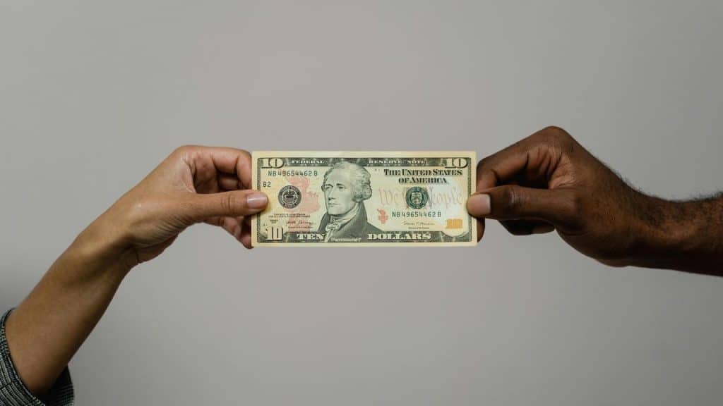 A pair of hands holding a ten dollar bill.