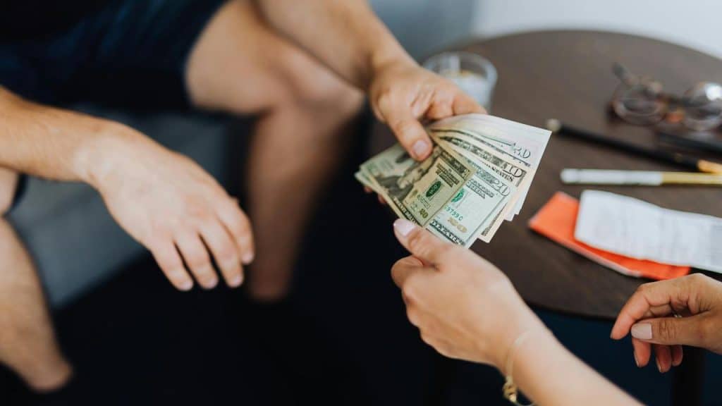 A person handing over a stack of US dollar bills to another person.
