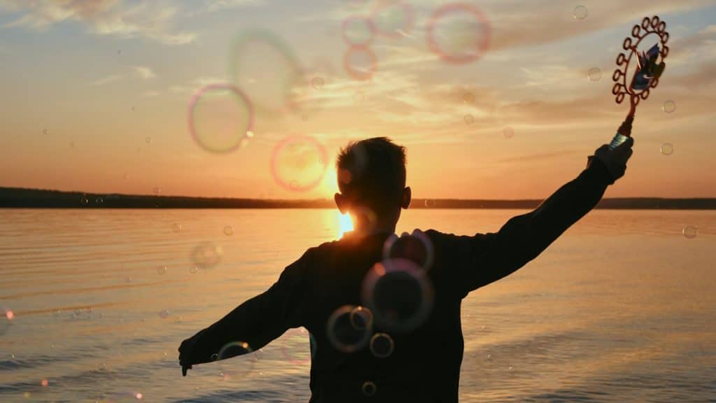 A young man blows bubbles in the sunset.