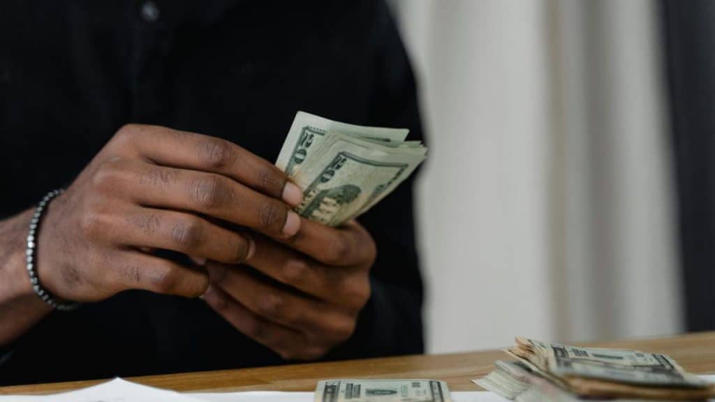 A person counting a stack of US dollar bills.