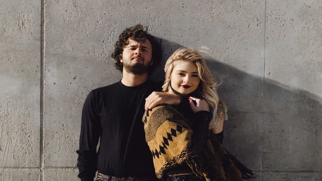 A man and a woman leaning against a wall.