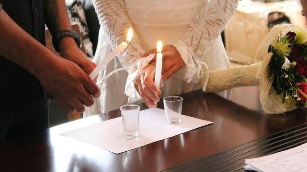 A couple lighting candles in front of a table.