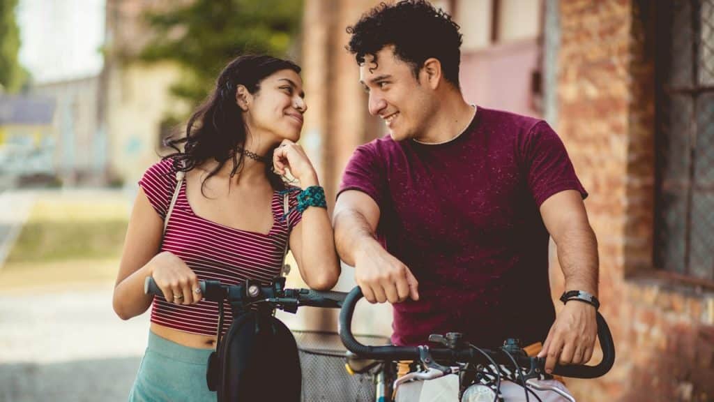 A young couple on the street with a bike and a scooty.