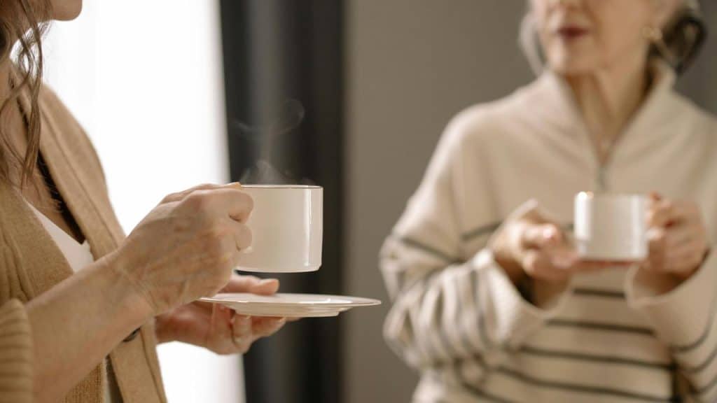 A close-up of two people holding cups of coffee while talking.