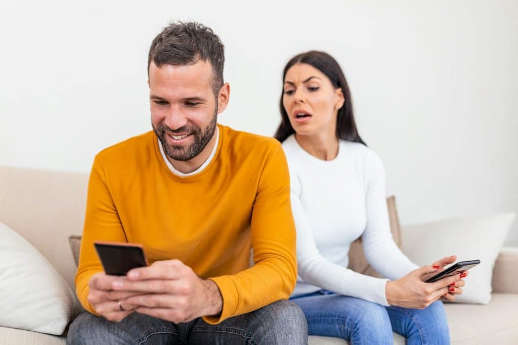 The woman secretly reads the message from her man’s phone.