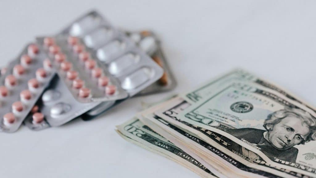 A stack of US dollar bills next to blister packs of pills.