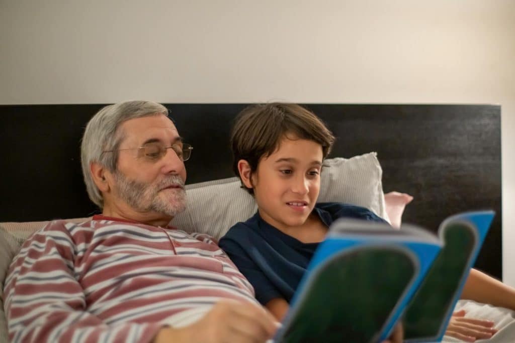 A man and his kid reading books in the bed.
