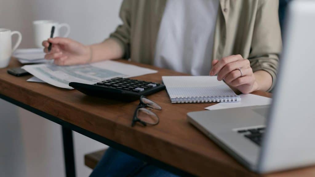 A person working at a desk with papers, a calculator, and a laptop.