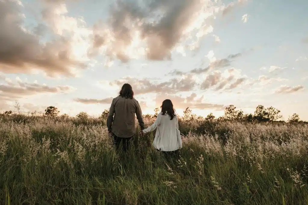 A man and a woman walking in the fields hand to hand.