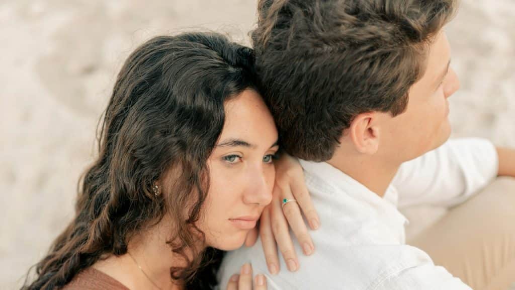 A woman leaning on her man’s back with a sad expression.