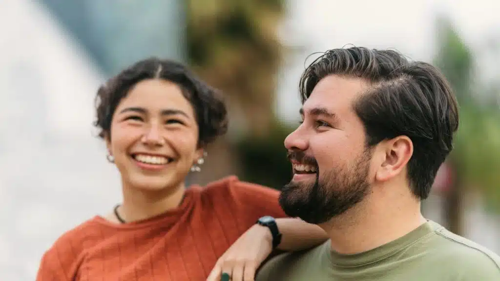 A smiling couple with the woman having her arm placed on the man’s shoulder.