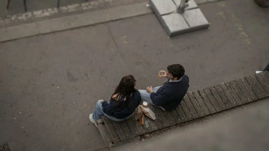 A couple talking while sitting on a bench outdoors and having coffee.