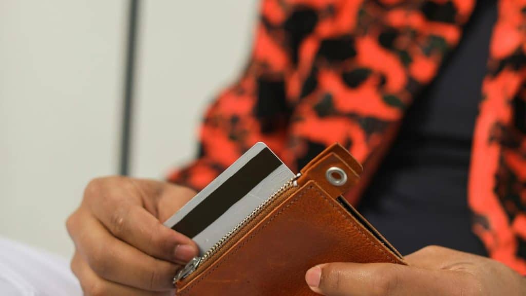 A person holding a credit card and a brown wallet.