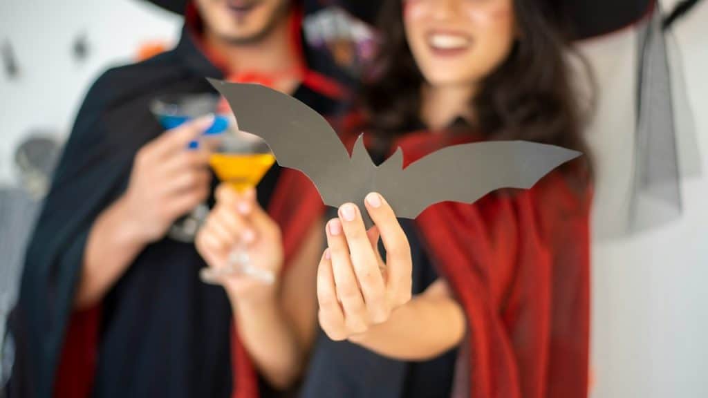 A couple wearing costumes with the girl holding out a cut-out paper bat.
