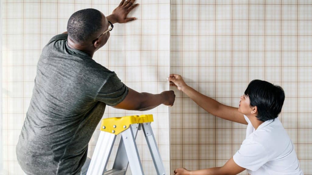 A couple putting up wallpaper on a wall in their home.