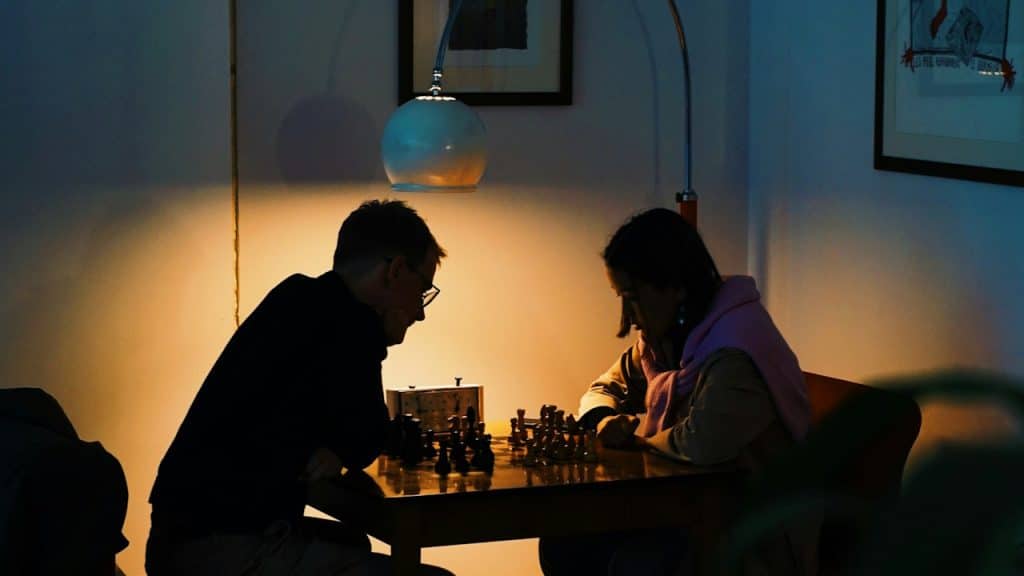 A couple playing chess in the dimly lit room.