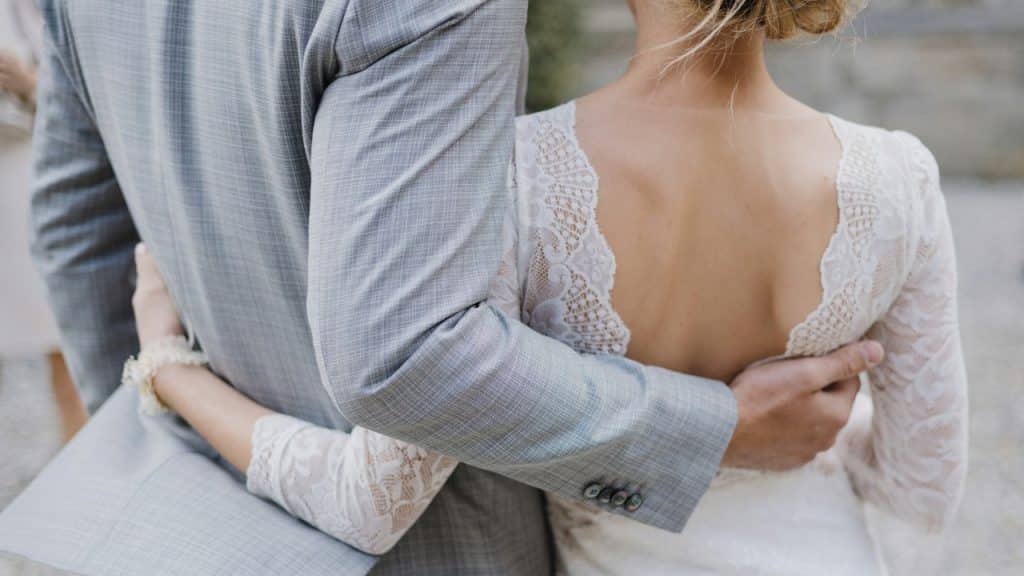 A close-up of a bride and groom hugging from the back, showing the groom's arm around the bride's waist.