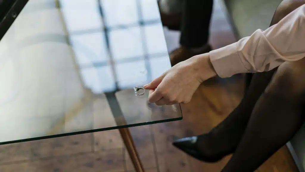 A person placing a wedding ring on a glass table.