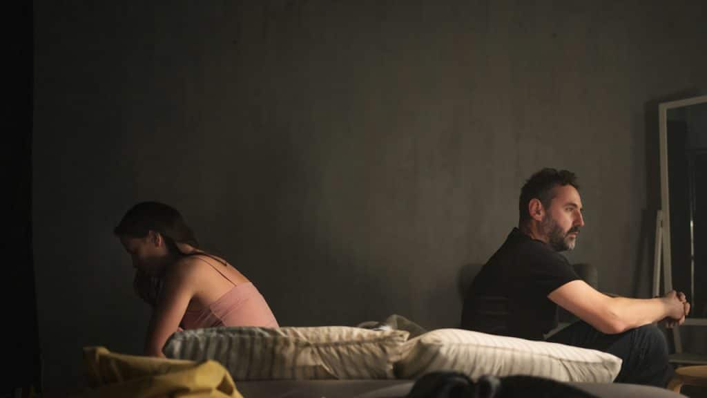 Betrayed woman with her husband sitting back to back on bed.