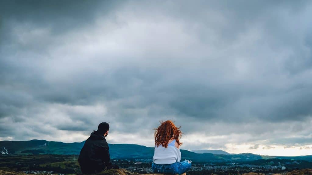 A man and a woman sitting on the top of a hill.