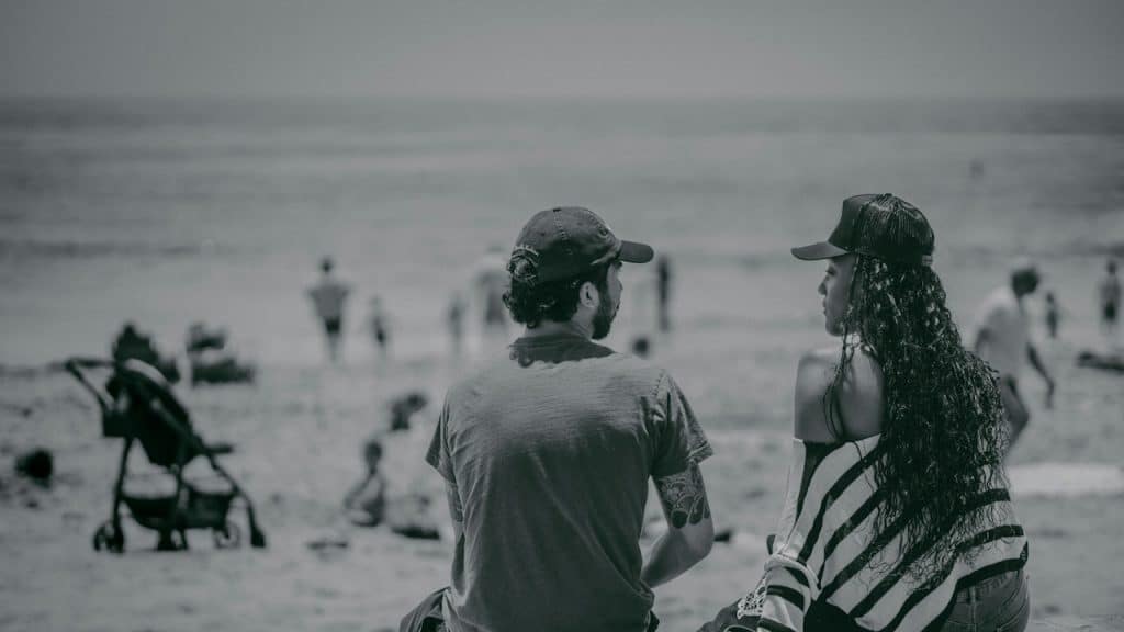 A man and a woman sitting on a pier looking at the beach.