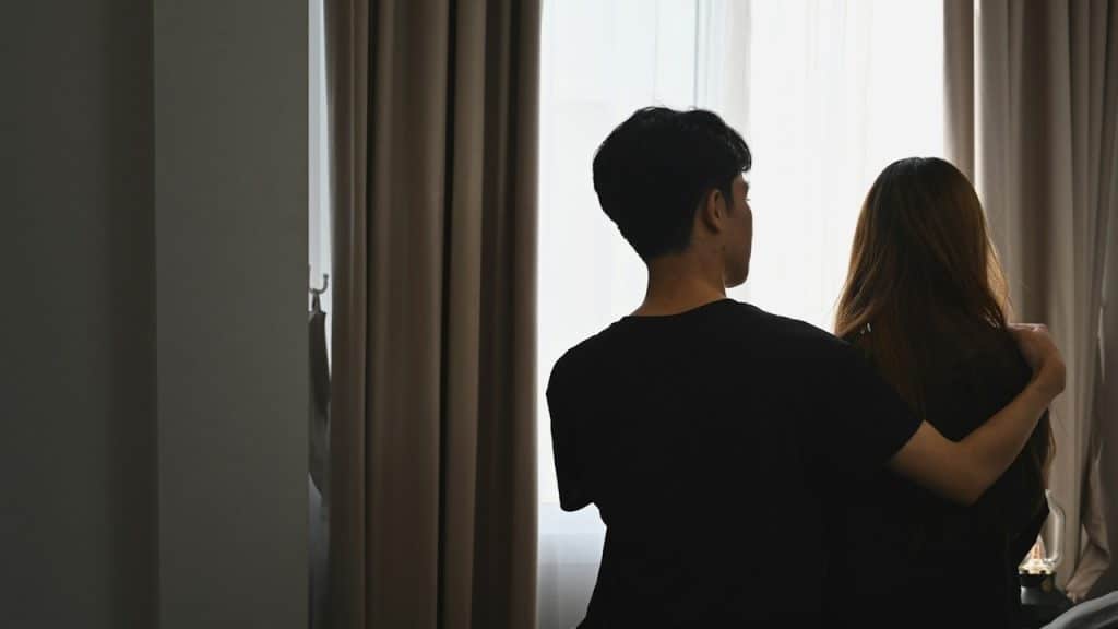 A man embracing his wife while sitting in the bedroom.