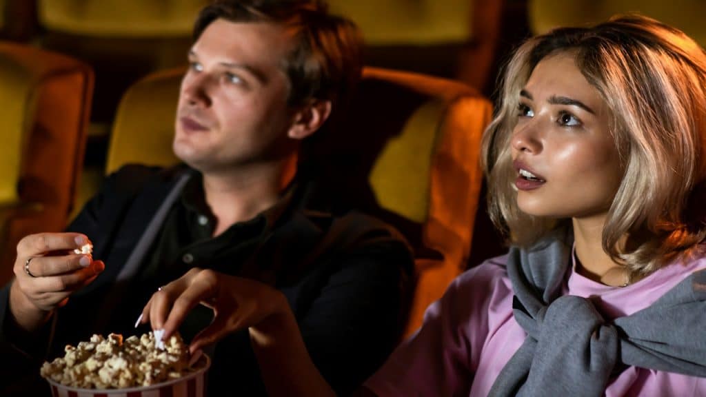 The couple enjoyed watching a movie and eating popcorn together in a cinema.