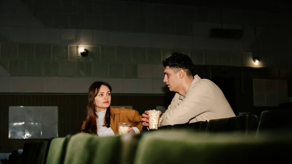 A couple eating popcorn while sitting in a cinema.