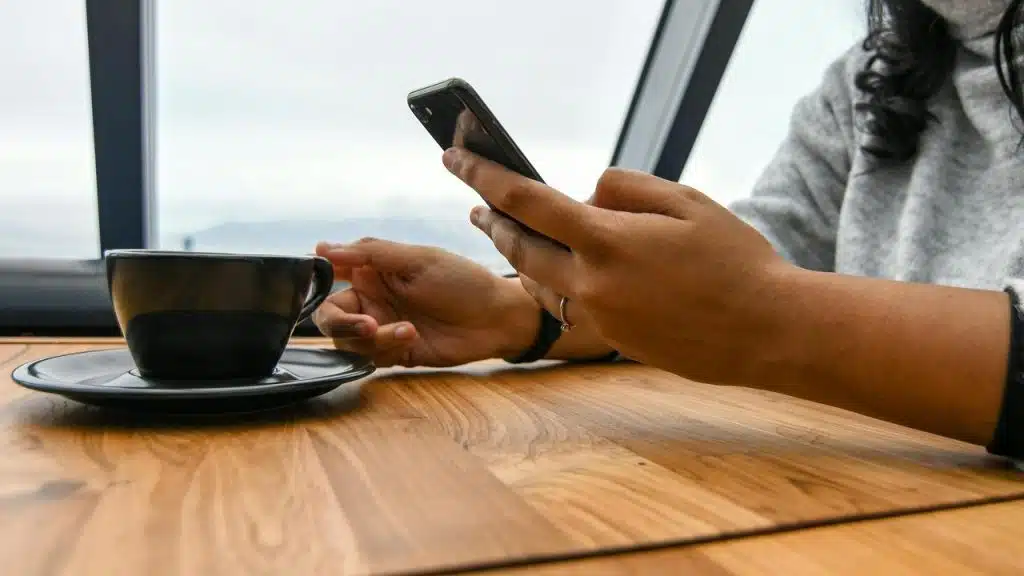 A person holding a smartphone while sitting at a table with a cup of coffee.
