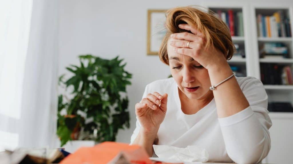 A woman sitting at a table looking stressed with her hand on her forehead.