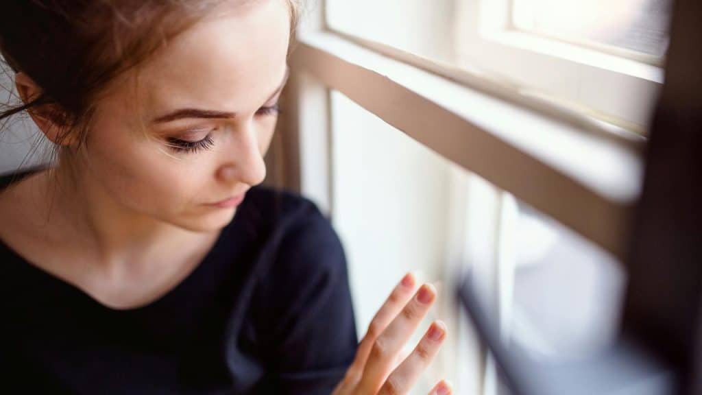 A woman in a black top looking down while touching a window.