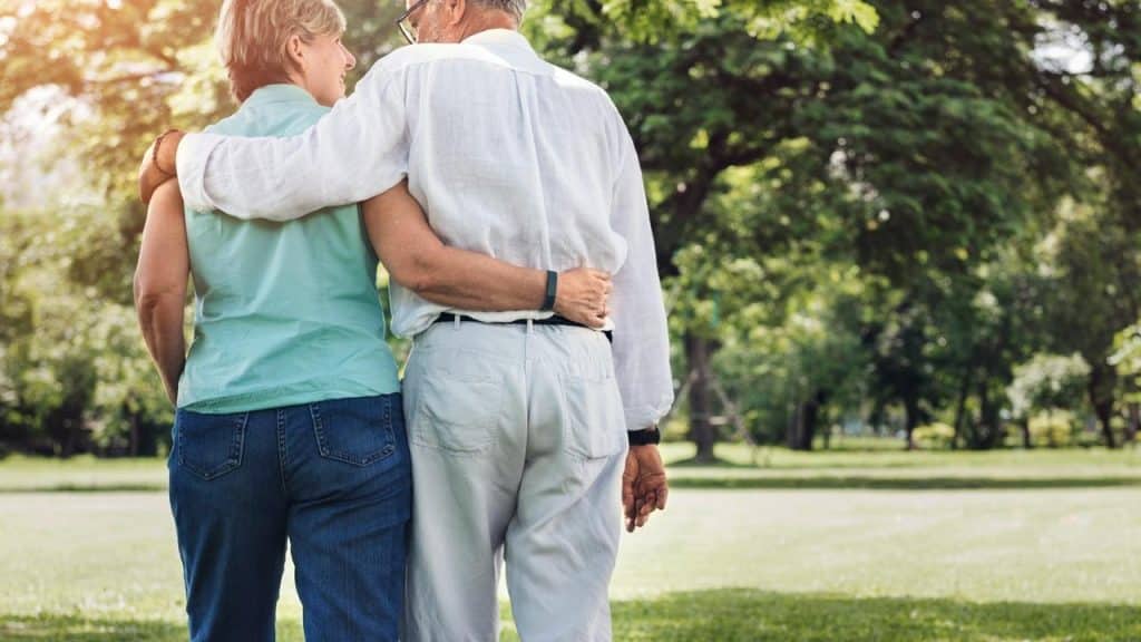 An elderly couple walking arm in arm through a park.
