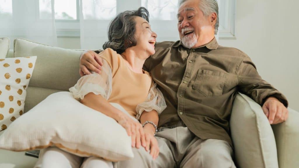 An elderly couple sitting on a couch laughing together.