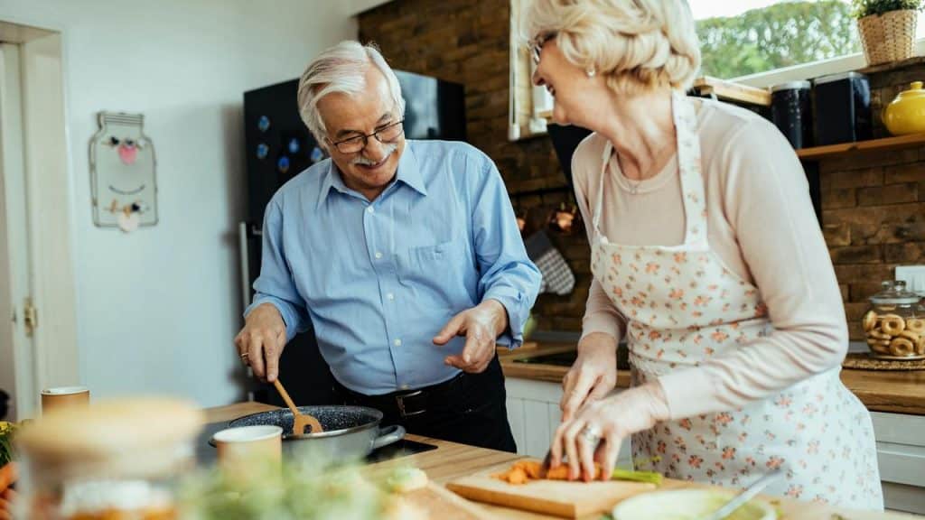 An elderly couple cooking together and smiling in the kitchen.
