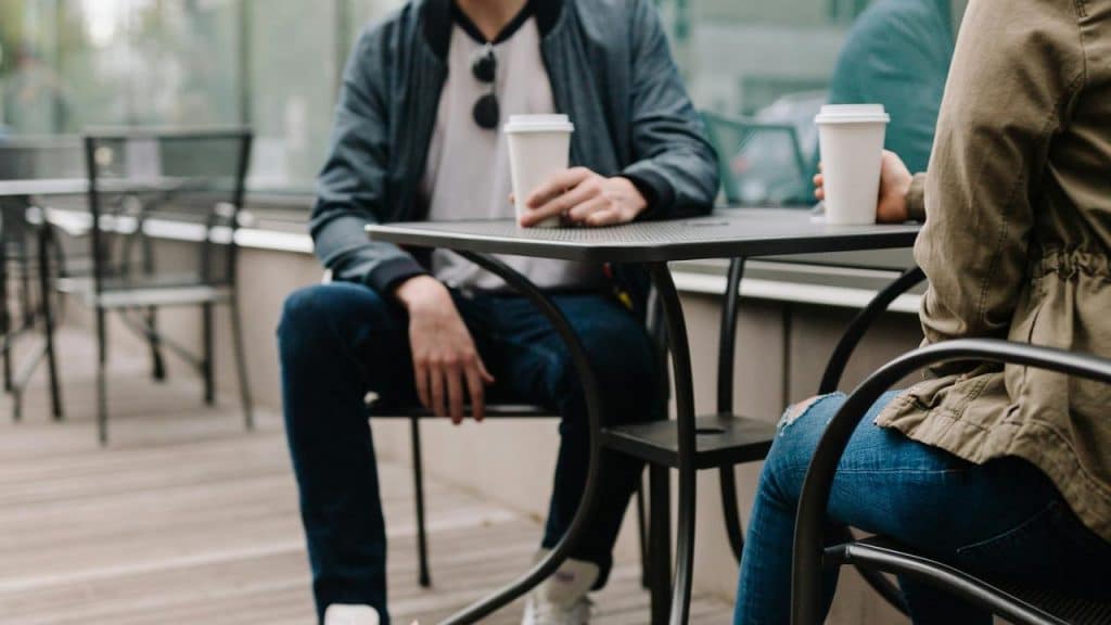 A photo of two people sitting at an outdoor café table holding coffee cups.