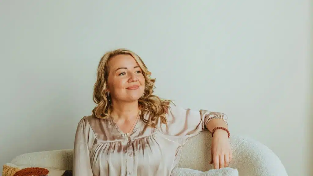 A woman sitting on a couch smiling and looking to the side.