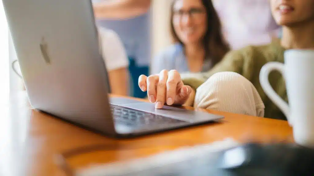 A person using a laptop with friends in the background.