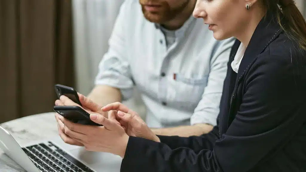 A man and a woman discussing something while looking at their phones.