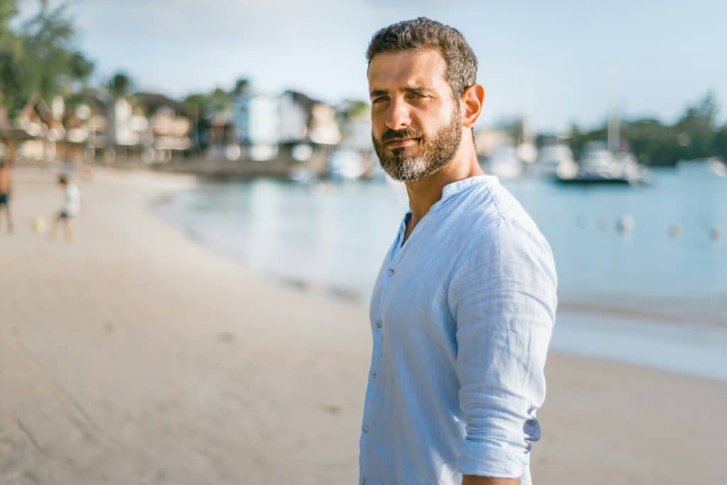The man is exuding confidence while standing on a beach in the daytime.